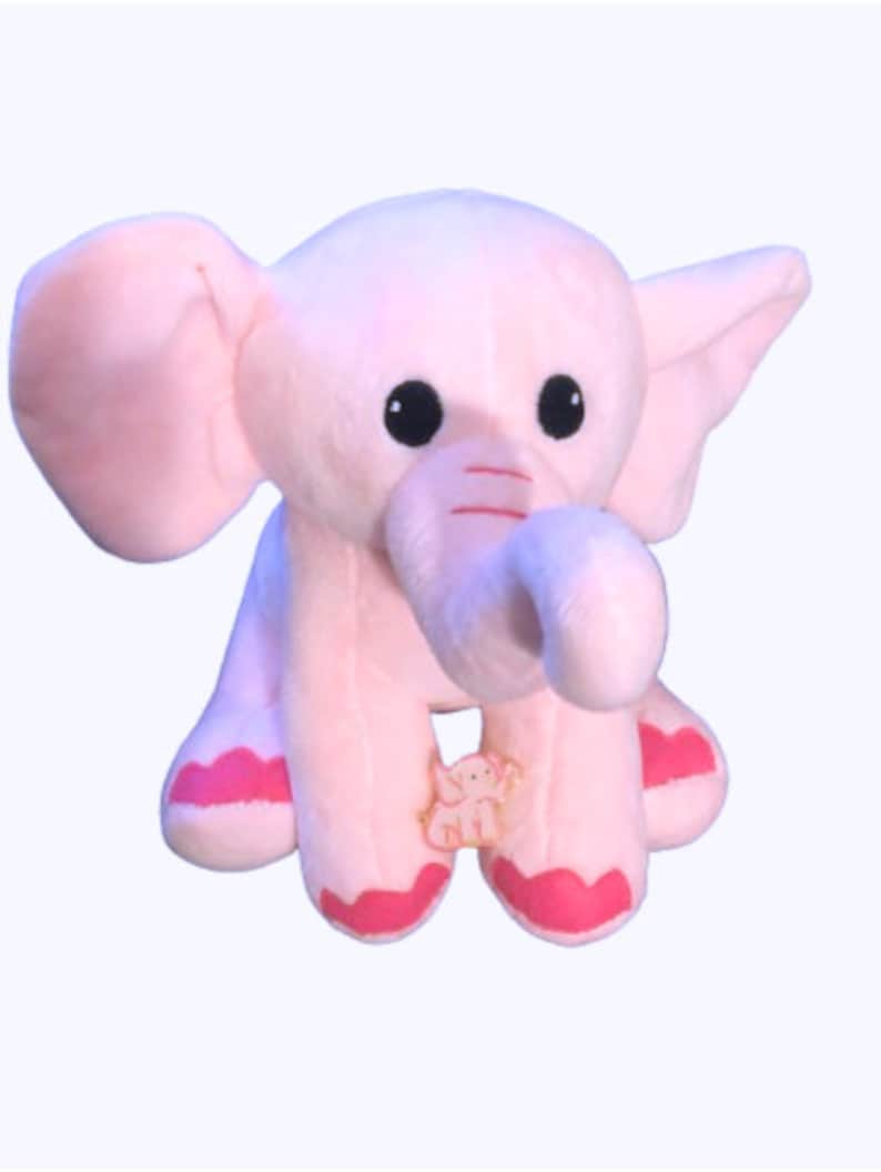 May include: A pink plush elephant toy with large ears, a long trunk, and black eyes. The elephant has pink accents on its feet and a small elephant design on its belly.