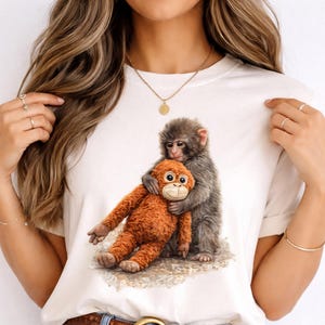 以下が含まれることがあります： 2匹のサルが抱き合っているグラフィックが特徴の白いTシャツ。1匹はグレー、もう1匹はオレンジ色です。デザインは中央に配置され、遊び心があり心温まるイメージを作り出しています。シャツは柔らかく快適な素材で作られています。
