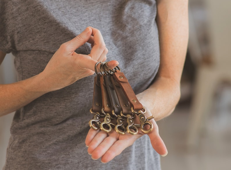 May include: A set of six leather keychains with brass key rings and clips. The keychains are in various shades of brown.