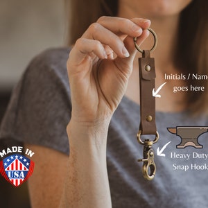 May include: A brown leather keychain with a heavy-duty snap hook and a space for initials or a name. The keychain is made in the USA. "Made in USA" is printed on a red, white, and blue shield.