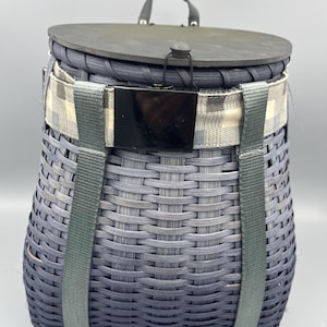 May include: A blue woven wicker basket with a black leather handle and a black and white checked strap. The basket has a wooden lid and two green straps.