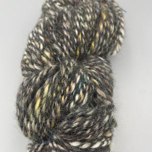 May include: A skein of black yarn with white, brown, and yellow flecks. The yarn is soft and fluffy, and it would be perfect for knitting or crocheting.