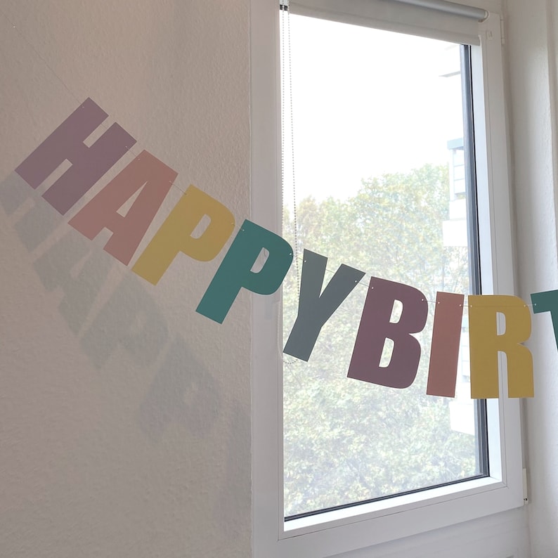 May include: A colourful paper banner with the words "Happy Birthday" hanging in a window.
