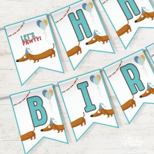 Può includere: Uno striscione colorato con le parole "Let's Pawty!" e le lettere "Happy Birthday" in turchese. Ogni lettera è decorata con un bassotto che indossa un cappello da festa e un palloncino.