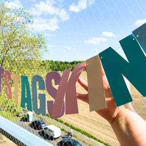 May include: A colourful paper banner with the words "Geburtstagskind" strung across a white net. The banner is made of individual letters in different colours, including pink, blue, green, and yellow.