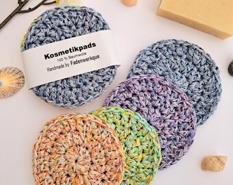 May include: Four crocheted cotton makeup remover pads in different colors: blue, purple, green, and orange. The pads are 100% cotton and handmade. The label reads "Kosmetikpads 100% Baumwolle Handmade by: Fadenwerkque".