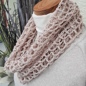 Könnte beinhalten: Ein hellrosa gehäkelter Schal mit einem hohen Kragen. Der Schal ist mit einem zarten Lochmuster gearbeitet.