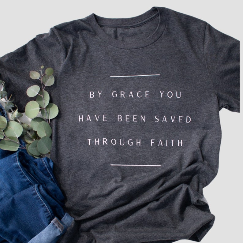 K&ouml;nnte beinhalten: Ein dunkelgraues T-Shirt mit dem Aufdruck "By grace you have been saved through faith" in wei&szlig;.