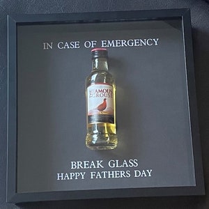 Puede incluir: Una imagen enmarcada con una botella en miniatura de whisky The Famous Grouse en su interior. El marco tiene el texto "En caso de emergencia, romper el vidrio, Feliz Día del Padre."