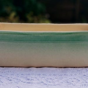 May include: A rectangular ceramic planter with a light green glaze that fades to a cream colour. The planter has a smooth, glazed finish.
