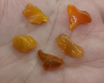 May include: Five polished, orange-yellow opal gemstones with iridescent flashes are displayed in a hand. The opals have irregular shapes and varying sizes, showcasing their natural beauty. The gemstones are translucent and appear to glow.