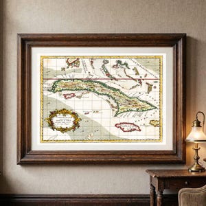 Op de afbeelding: Een ingelijste kaart in antieke stijl van Cuba en de omliggende eilanden, voorzien van een decoratieve cartouche met tekst, een raster en handgekleurde topografische details, gevat in een donkerbruine houten lijst met een witte passe-partout.