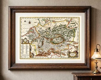 Op de afbeelding: Een ingelijste antieke kaart van Germanië met gedetailleerde cartografie, een windroos en decoratieve illustraties. De kaart zit in een donkerbruine houten lijst met een witte passe-partout en toont historische geografische labels en tekst.