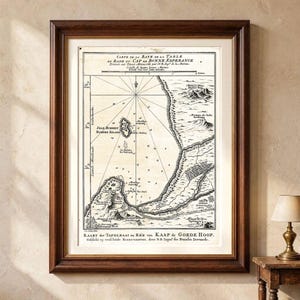 Könnte beinhalten: Eine gerahmte historische Seekarte mit dem Titel Carte de la Baye de la Table et Rade du Cap de Bonne Esperance, mit schwarzer Tinte auf cremefarbenem Hintergrund. Die Karte zeigt Küstentopografie, eine Windrose sowie niederländischen Text.