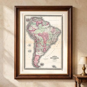 Puede incluir: Un mapa antiguo enmarcado de América del Sur con regiones codificadas en colores verde y rosa pastel, etiquetas de texto en negro y un borde decorativo. El mapa incluye el texto Johnson's South America publicado en Nueva York en un marco de madera.