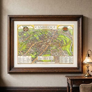 May include: A framed pictorial map of Cambridge featuring a detailed street layout in shades of green, yellow, and brown. The map includes the title CAMBRIDGE, a compass rose, and three distinct legend boxes listing colleges, churches, and buildings.