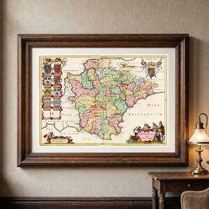 Puede incluir: Un mapa antiguo enmarcado de Devon, Inglaterra, que presenta regiones coloreadas a mano, una columna de escudos heráldicos a la izquierda, un cartucho decorativo con el texto "DEVONIA" abajo a la derecha y un escudo real arriba a la derecha.