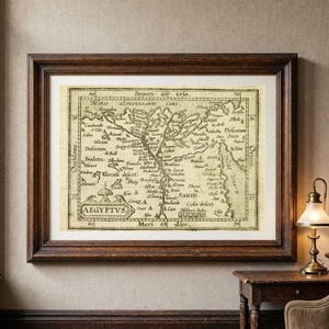 Może przedstawiać: Oprawiona w ramę antyczna mapa Egiptu z napisem AEGYPTVS, przedstawiająca szczegółowe linie kartograficzne, historyczne nazwy miejsc i oznaczenia geograficzne wykonane czarnym tuszem na kremowym tle, w ciemnobrązowej drewnianej ramie.