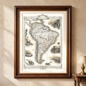 Puede incluir: Un mapa de estilo antiguo enmarcado de América del Sur con detallados dibujos lineales en blanco y negro de paisajes, animales y personas en los márgenes. El mapa está dentro de un marco de madera marrón oscuro con un paspartú color crema.