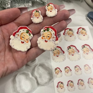May include: A collection of vintage Santa Claus-themed craft supplies. The image shows several Santa Claus face cutouts, a sheet of Santa Claus stickers, and Santa Claus-shaped molds. The Santa faces have red hats and white beards.