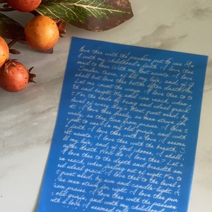 May include: A blue stencil with white cursive text. The text is a poem about love. The stencil is on a white surface with orange berries and green leaves in the background.