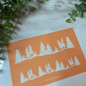May include: An orange card features a white forest silhouette design. The design includes multiple pine trees and a mountain range. The text "LunarLove Design Co" is printed in the bottom right corner. The card is on a white and gray marble surface.