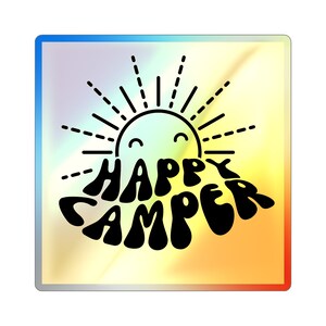 Puede incluir: Un diseño gráfico colorido con un sol sonriente y el texto "Happy Camper" en una fuente retro.