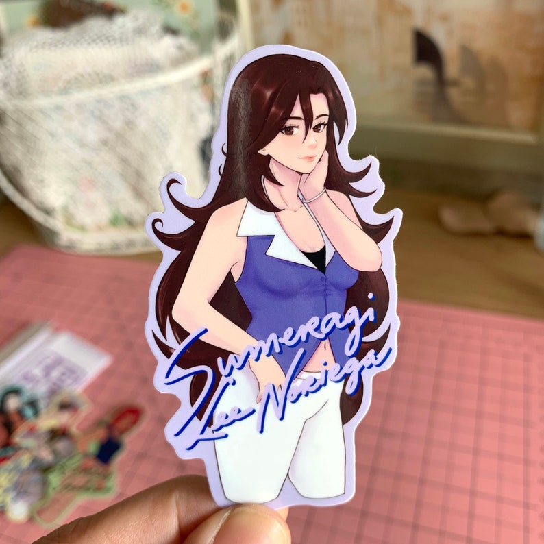 May include: A sticker featuring a cartoon illustration of a woman with long brown hair wearing a blue and white top and white pants. The sticker has a purple background and the text "Summeragi Lee Nariega" in blue.