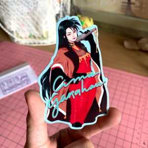 May include: A sticker featuring a woman with long black hair wearing a red and brown outfit holding a sword. The sticker has a blue border and the text "Cima Garahau" in blue.