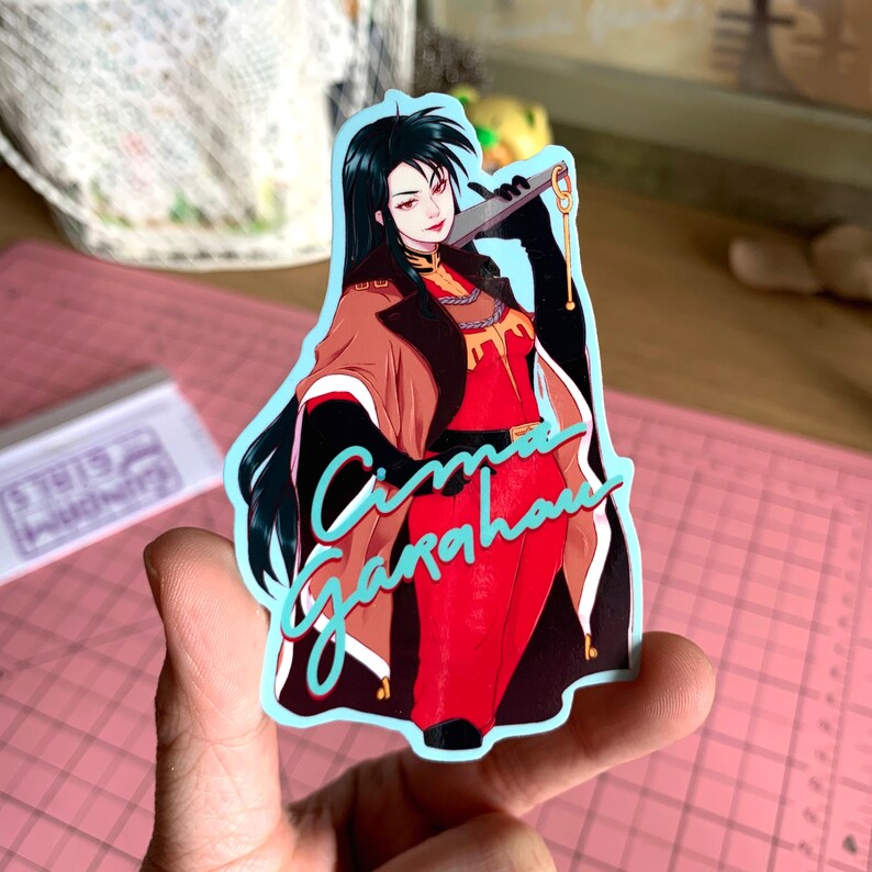 May include: A sticker featuring a woman with long black hair wearing a red and brown outfit holding a sword. The sticker has a blue border and the text "Cima Garahau" in blue.