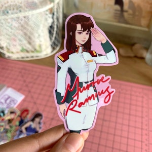May include: A pink background sticker featuring a cartoon anime character with brown hair, wearing a white and green uniform, saluting. The character's name is written in red cursive: "Murre Rameu".
