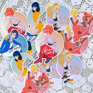 May include: A set of ten colorful round stickers featuring anime-style characters with different hairstyles and outfits. Each sticker has a unique design and text, including "Cargalli Yula Atha", "Biancar Carly", and "Modelia Aina Bernstein".