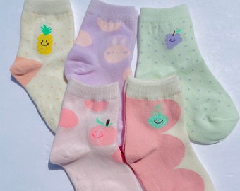 May include: Set of five colourful cotton socks with different fruit designs. The socks feature a pineapple, a peach, a pear, a grape, and a bunny.