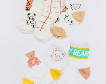 May include: Set of four white cotton socks with bear designs. One pair features a brown bear with a heart that says "Love Me". Another pair has a brown bear with a red bow tie. The third pair has a white bear with a green stripe and the text "My Bear". The last pair has a white bear with a brown stripe and a brown bear with a red bow tie.