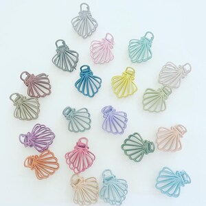 May include: Assortment of 18 pastel-colored plastic hair clips shaped like seashells. The clips are in various shades of blue, green, pink, purple, and brown.