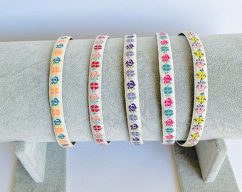 May include: Five white elastic hair ties with floral embroidery in different colours. The hair ties are displayed on a grey surface.