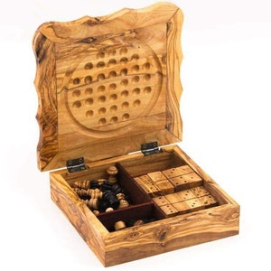 May include: Wooden game set with a variety of games, including chess and dominoes. The box is made of light brown wood and has a carved top with a solitaire game. The set is open, revealing the game pieces inside.