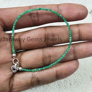 Puede incluir: Un brazalete de piedras preciosas verdes con un cierre de plata. El brazalete está hecho de pequeñas cuentas facetadas y mide aproximadamente 18 cm de largo.