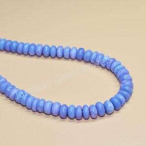 May include: A strand of light blue gemstone beads. The beads are round and have a slightly irregular shape. The beads are strung on a clear thread.