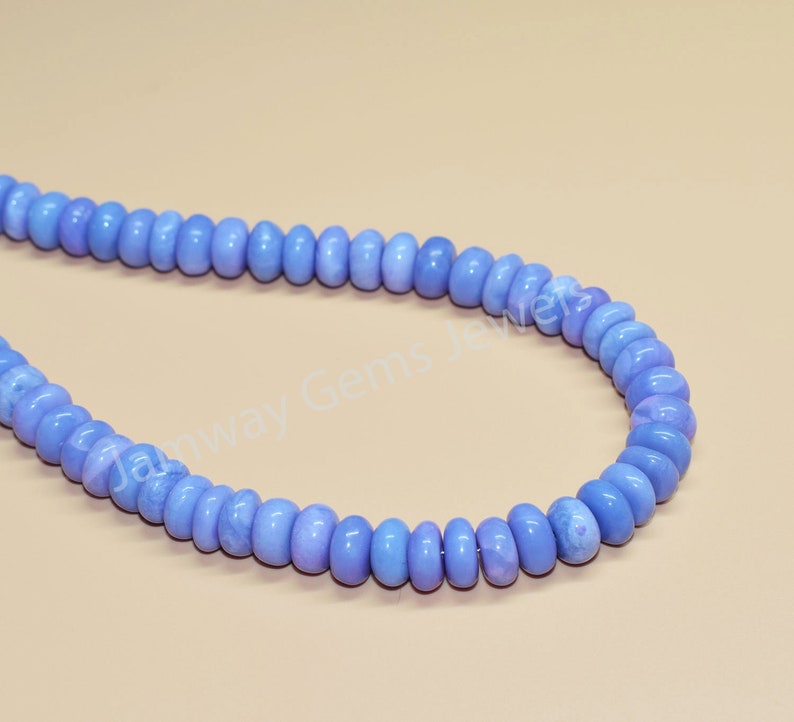 May include: A strand of light blue gemstone beads. The beads are round and have a slightly irregular shape. The beads are strung on a clear thread.