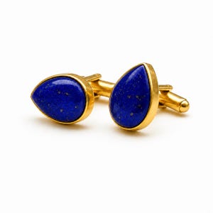 Puede incluir: Un par de gemelos con piedras de lapislázuli en forma de lágrima engastadas en metal dorado pulido. Cada gemelo tiene una superficie azul intenso con motas doradas naturales y un borde biselado liso y redondeado con cierre giratorio.