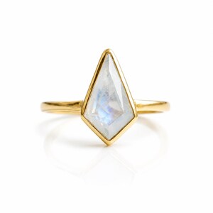 May include: A gold ring featuring a kite-shaped, iridescent gemstone. The gemstone is set in a gold bezel, and the band is a simple, polished gold. The ring is displayed on a white background, highlighting its elegant design.