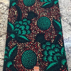 May include: A folded piece of fabric featuring a repeating pattern of large green circular shapes with textured black dots, surrounded by stylized green leaves and intricate red and yellow radiating lines on a deep black background.