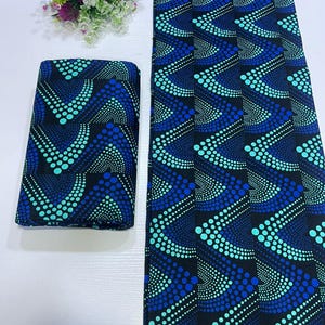 May include: A folded piece of fabric and a long strip of the same material, both featuring a black background with a repeating geometric pattern of blue and turquoise dots arranged in chevron-like waves, accompanied by a small floral bouquet.