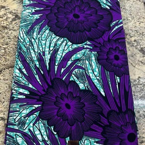 May include: A rectangular piece of fabric featuring a vibrant pattern of large, dark purple flowers with black outlines. The background consists of a teal and white marbled or crackled design, interspersed with long, dark purple, pointed leaves.