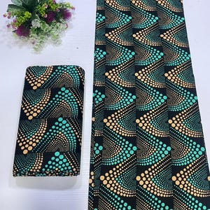 May include: A folded stack and a long, flat length of black fabric featuring a repeating geometric pattern of curved lines composed of small, vibrant teal and soft peach-colored dots arranged in a rhythmic, wave-like design across the surface.