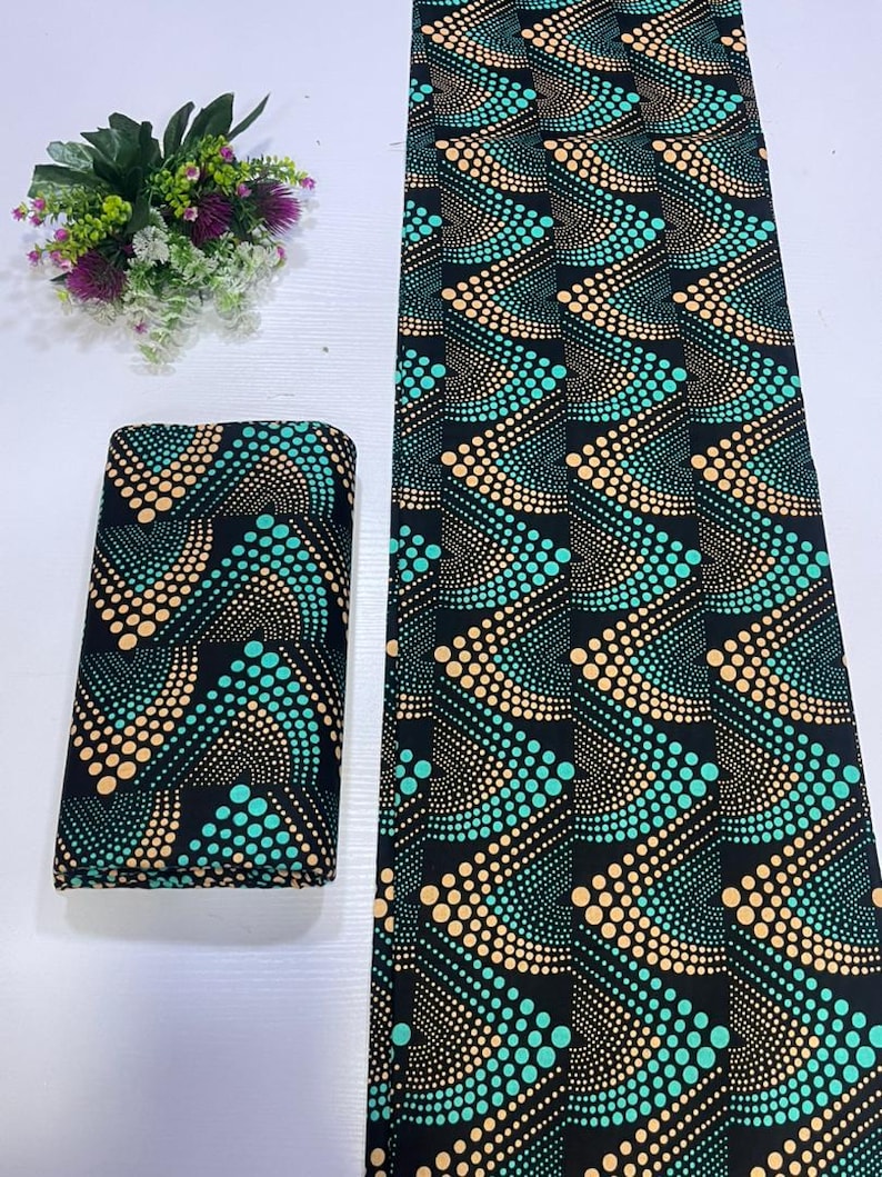 May include: A folded stack and a long, flat length of black fabric featuring a repeating geometric pattern of curved lines composed of small, vibrant teal and soft peach-colored dots arranged in a rhythmic, wave-like design across the surface.