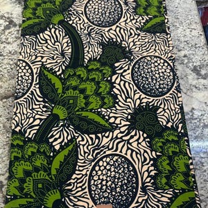 May include: A rectangular piece of fabric featuring a repeating pattern of large green and black floral motifs interspersed with circular dotted shapes against a cream background with swirling lines. The bottom edge displays the text V317408.