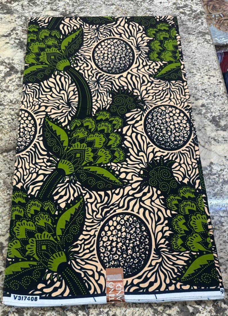 May include: A rectangular piece of fabric featuring a repeating pattern of large green and black floral motifs interspersed with circular dotted shapes against a cream background with swirling lines. The bottom edge displays the text V317408.