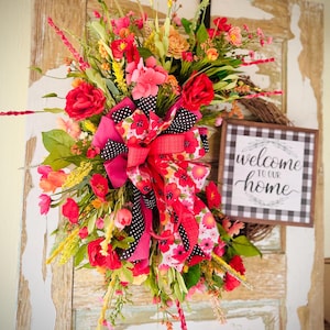 May include: A pink and red floral wreath with a black and white checkered sign that says "Welcome to our home".